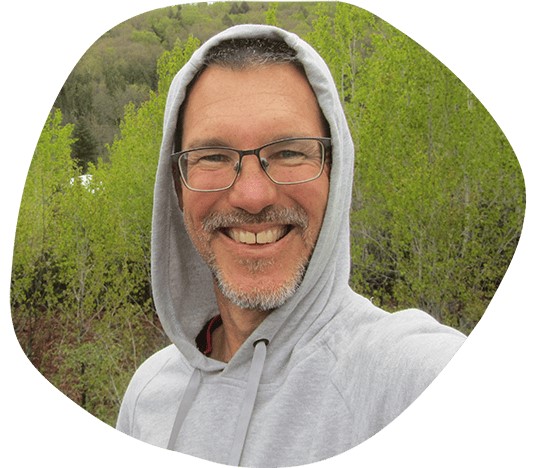Headshot of Jimmy Videle smiling towards the camera. Wearing a grey hoodie with the hood up - and glasses.