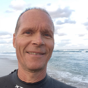 Jonathan Balcombe headshot. Standing on a beach with the sea in the background. Wearing a wetsuit.