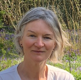 Head and shoulders shot of Denise Baden looking towards the camera, standing outside with grass and trees in the background.